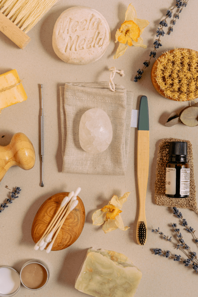 A mixture of travel-size toiletries, including a toothbrush, soap, Q tips, a scrub brush, some flowers, and a stone.