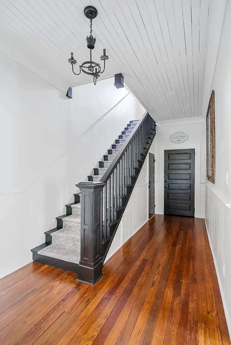 Wood staircase with white carpet runner and rich wood flooring in entryway