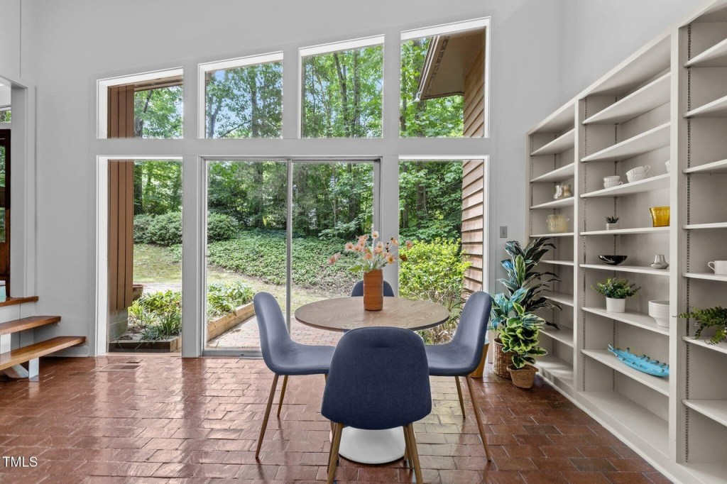 Open-concept mid-century dining area with built in bookshelves and clerestory windows and brick floors.
