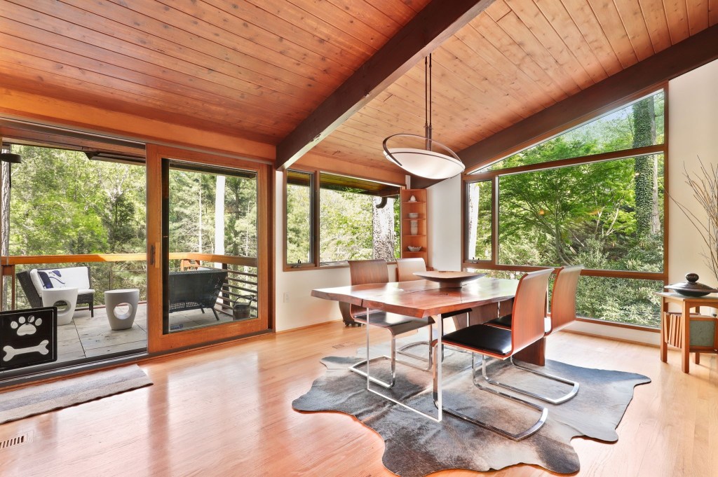 Open-plan living and dining space with retro decor and forest-facing windows

