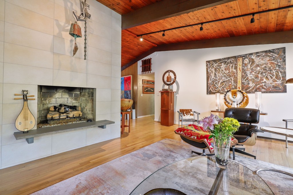 Open-plan living space with retro decor and forest-facing windows and a cozy white stone fireplace.
