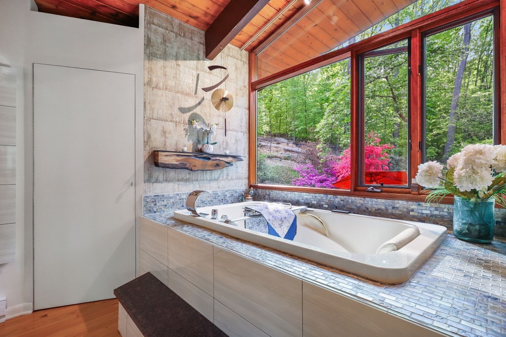 Vintage mid-century bathroom with spa bath and wood ceiling and big bright open windows with garden view

