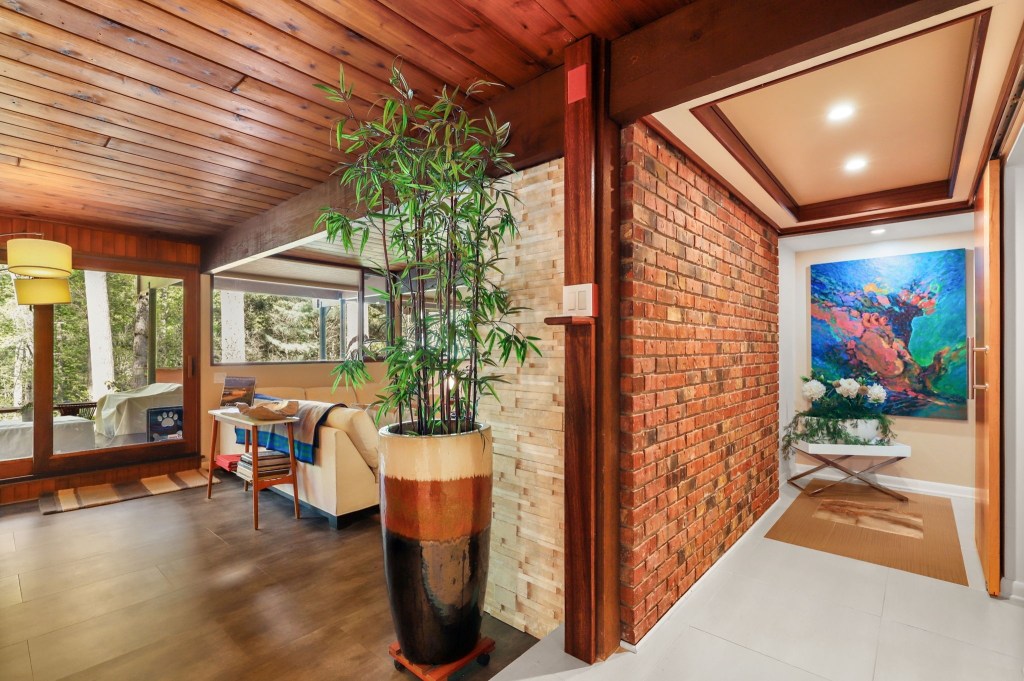 Open-plan living space with retro decor and forest-facing windows and brick wall

