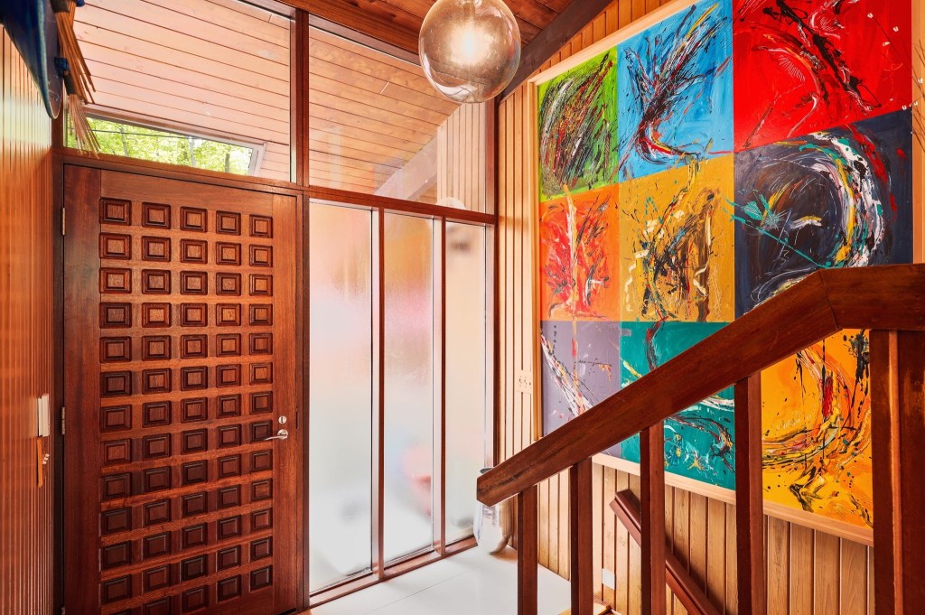 An entryway of a mid-century modern house with clerestory windows above the door frame and a split-level staircase.