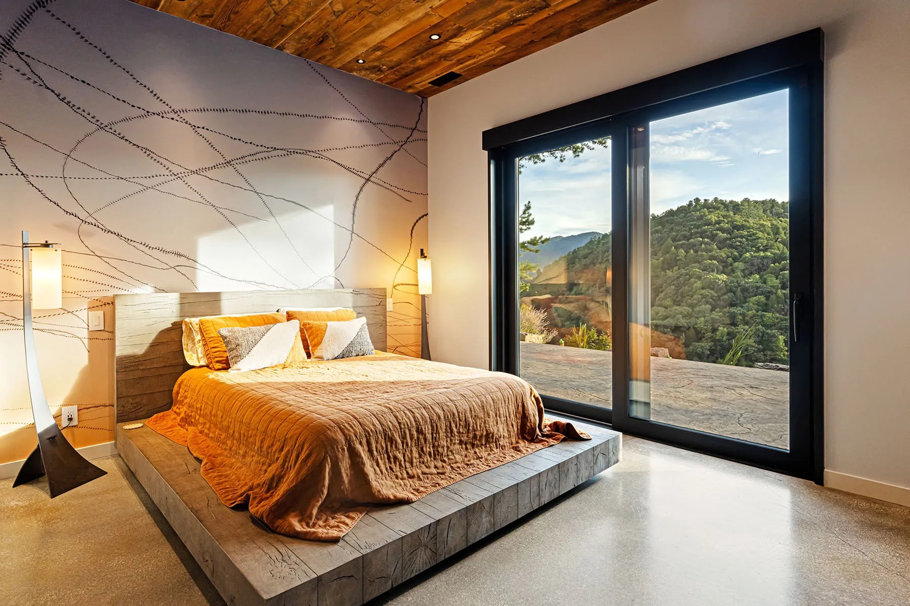 Cozy bedroom with large windows showcasing the wooded setting of this green home

