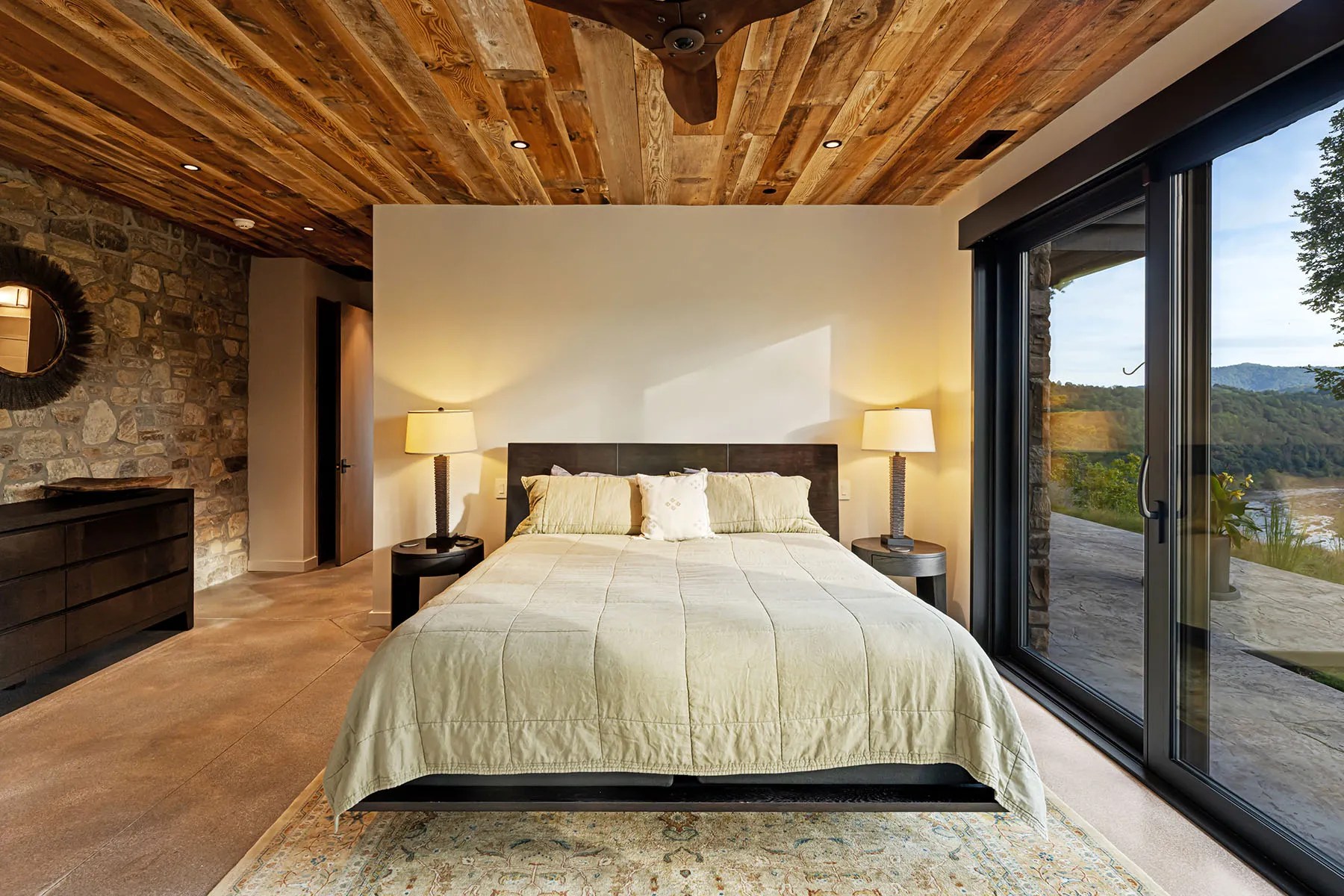 Cozy bedroom with large windows showcasing the wooded setting of this green home

